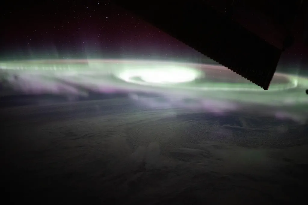 Aurora austral fotografada da Estação Espacial Internacional: uma faixa verde abraçando o horizonte, com cortinas magenta subindo dela para um céu estrelado.